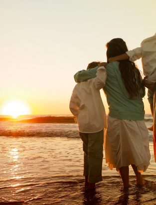 A family hugging each other while standing on the beach surrounded by the sea during the sunset