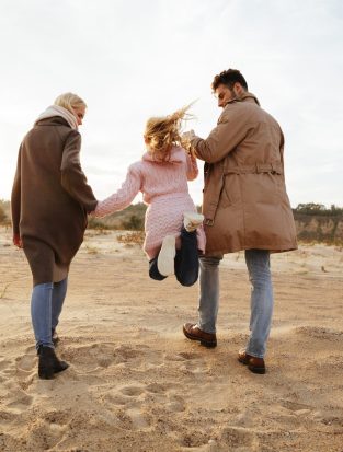 Portrait of a beautiful family with a little daughter having fun while walking along the beach together holding hands